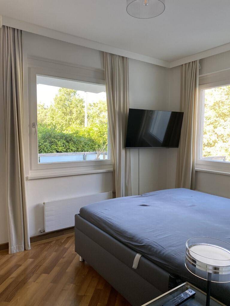 Schlafzimmer mit Doppelbett, Wandfernseher, Holzboden und Blick ins Grüne.