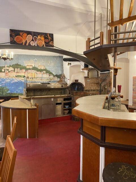 Geräumiger Restaurantbereich mit einer Bar, einem großen Pizzaofen und einer Wandmalerei, die eine Küstenstadt darstellt.