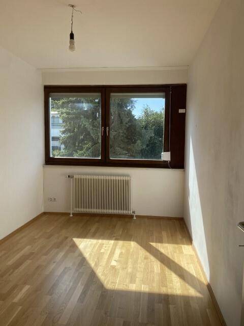 Heller Raum mit Parkettboden, großem Fenster und Blick ins Grüne, ideal als Schlafzimmer.