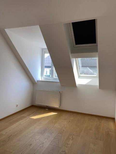 Gemütliches Schlafzimmer mit Dachschrägen, Holzboden und zwei Fenstern für viel Tageslicht.