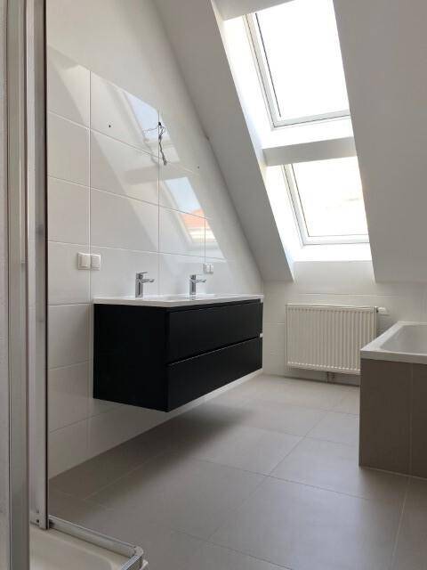 Modernes Badezimmer mit Doppelwaschbecken, Badewanne, Fliesen und hellen Dachfenstern.