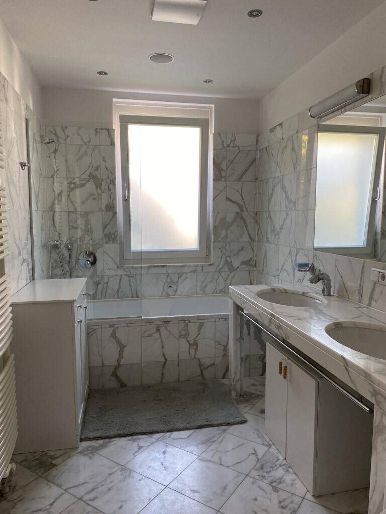 Modernes Badezimmer mit Marmorfliesen, Doppelwaschbecken, Badewanne und Fenster.