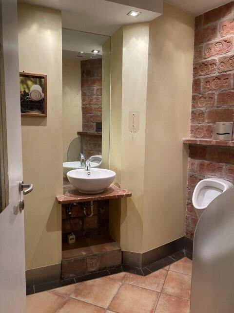 Badezimmer mit einem modernen Waschbecken, einem Urinal und gefliestem Boden, ausgestattet für Gäste.