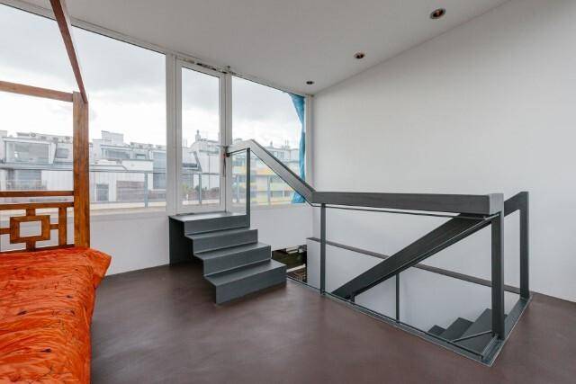 Helles Schlafzimmer mit großen Fenstern, Blick auf die Stadt und moderner Treppe zum oberen Bereich.