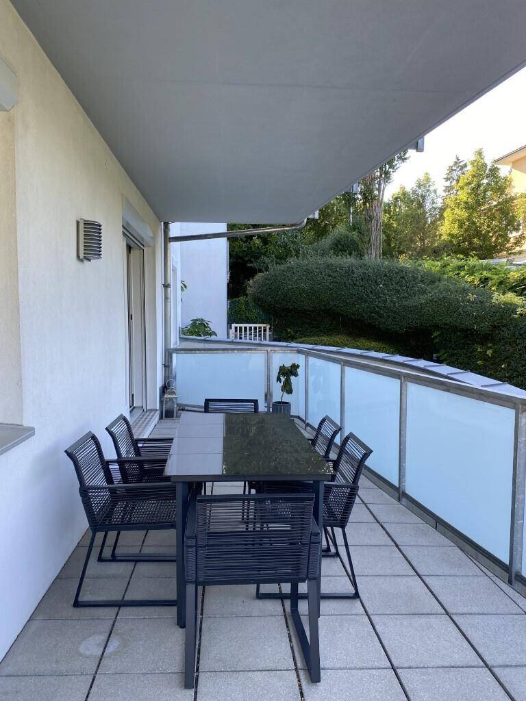 Geräumiger Balkon mit Esstisch und Stühlen, umgeben von üppigem Grün.