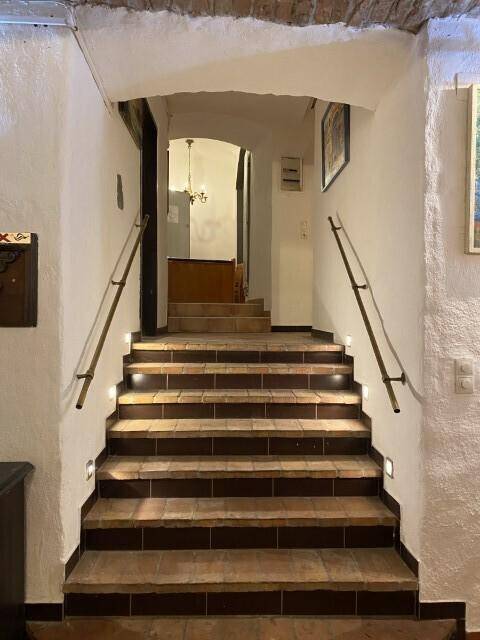Beleuchtete Treppe mit Handläufen und gefliesten Stufen, die zu einem oberen Bereich des Gebäudes führt.