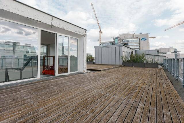 Geräumige Dachterrasse mit Holzbelag und Blick auf die umliegende Stadtlandschaft und Gebäude.