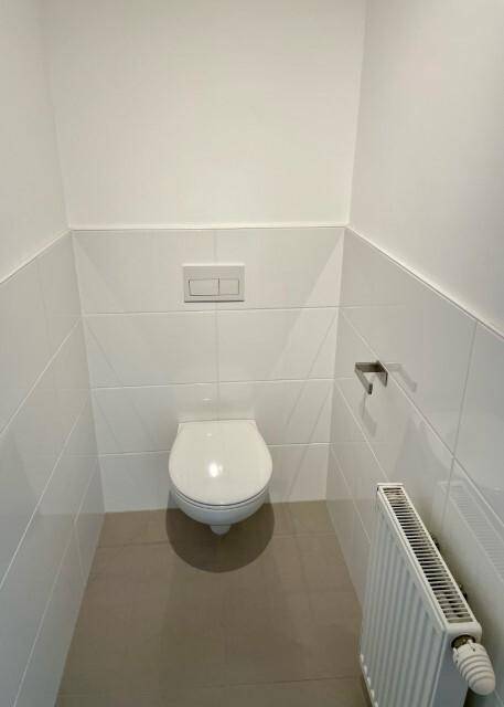 Modernes Gäste-WC mit wandhängendem WC, weißen Fliesen und Heizkörper.