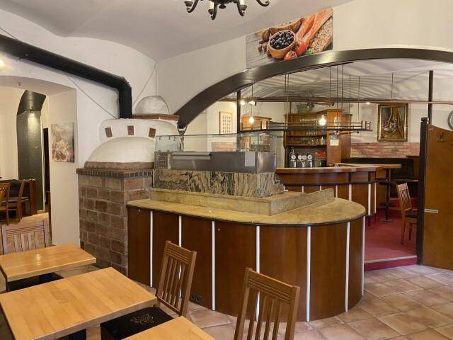 Innenansicht eines Restaurants mit einem traditionellen Pizzaofen, einer Theke und gefliestem Boden, bereit für den Betrieb.