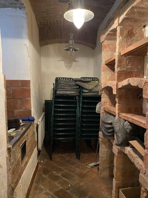 Lagerraum mit gestapelten Stühlen, Ziegelregalen und gefliestem Boden, genutzt für Restaurantbedarf.