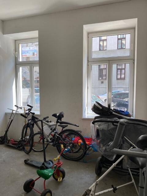 Heller Fahrradraum mit Fenstern und Abstellmöglichkeiten für Fahrräder und Kinderwagen.