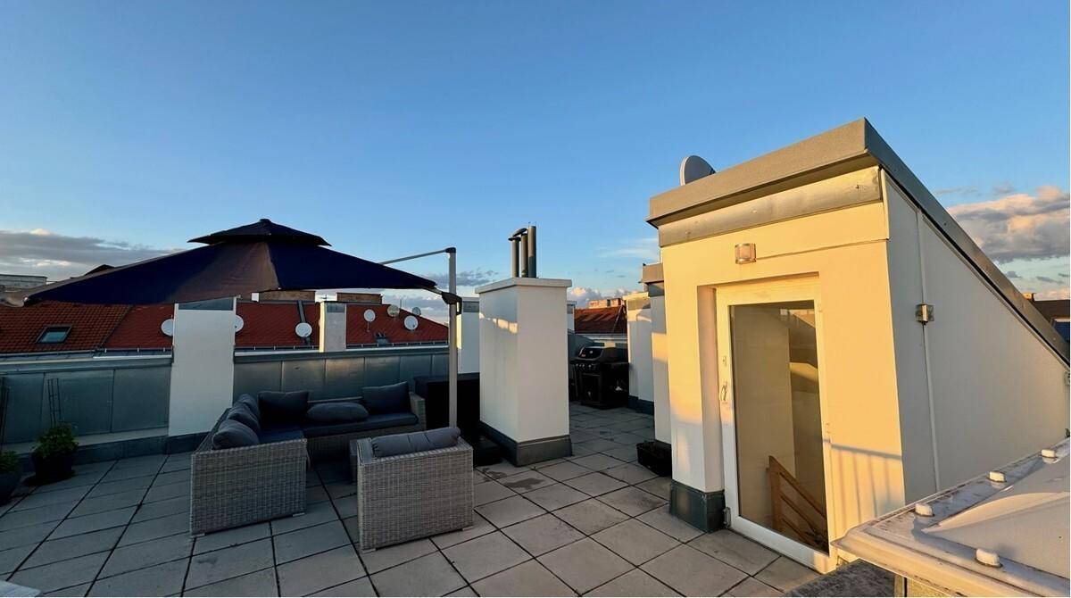 Dachterrasse bei Sonnenuntergang mit Loungemöbeln und Zugang zum Innenbereich.