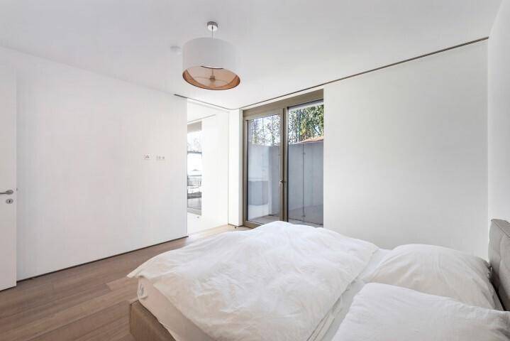 Helles Schlafzimmer mit schlichtem Design, Holzboden und Fensterfront, die viel Licht hereinlässt.