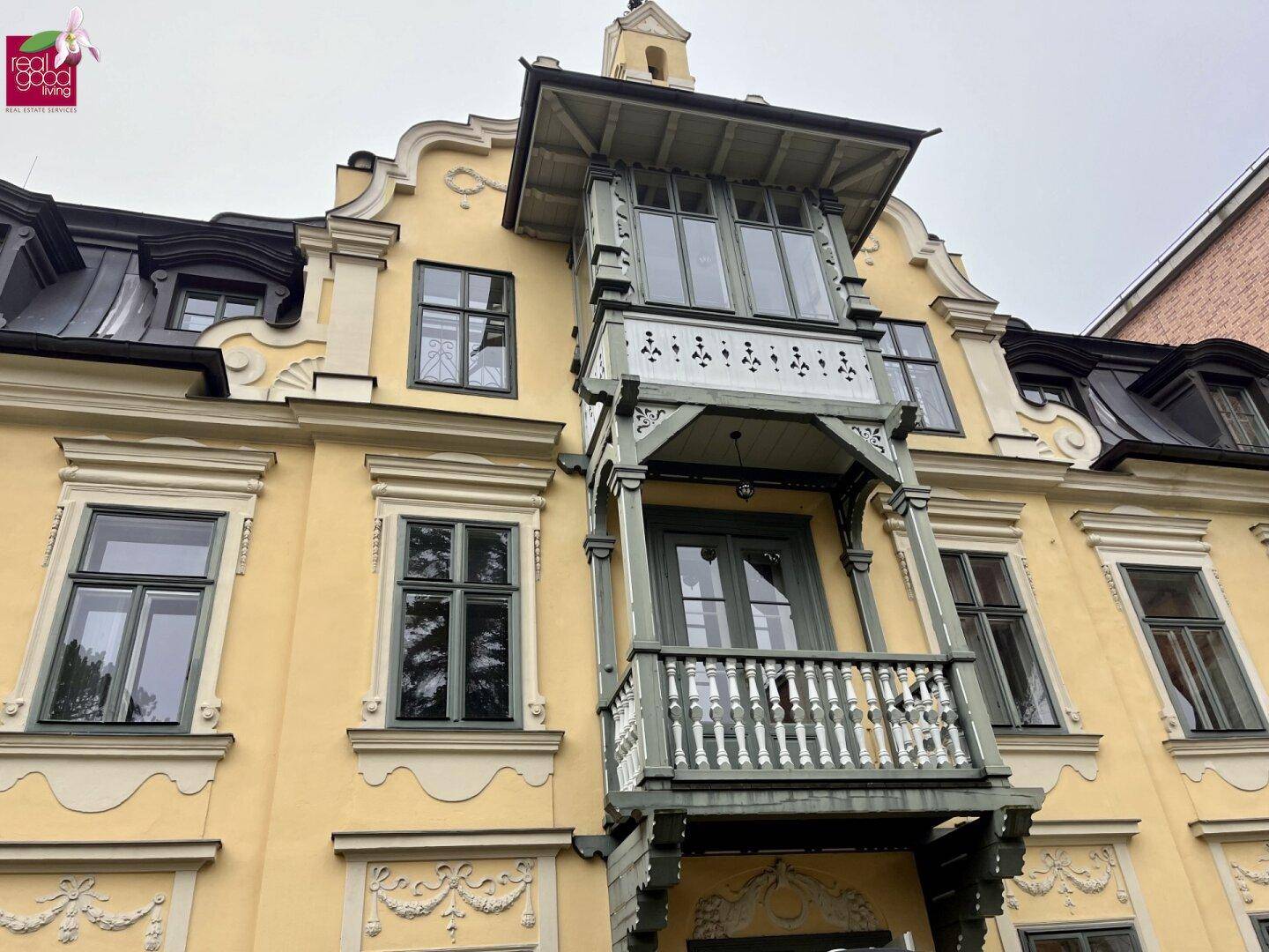 Detailansicht der historischen Fassade mit kunstvollem Balkon und verzierten Fenstern.