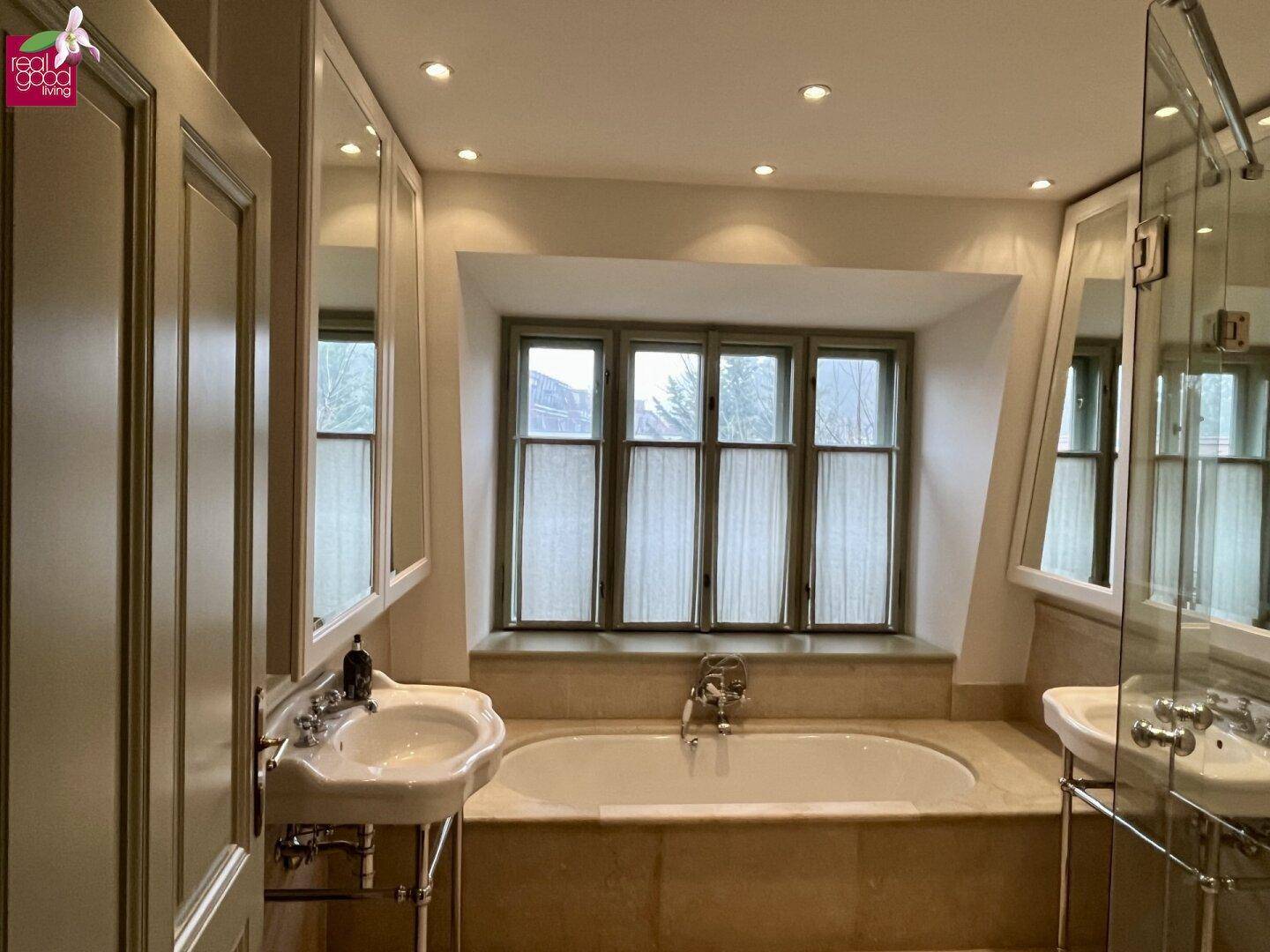 Elegantes Badezimmer mit Einbaubadewanne, Doppelwaschbecken und Fenster.
