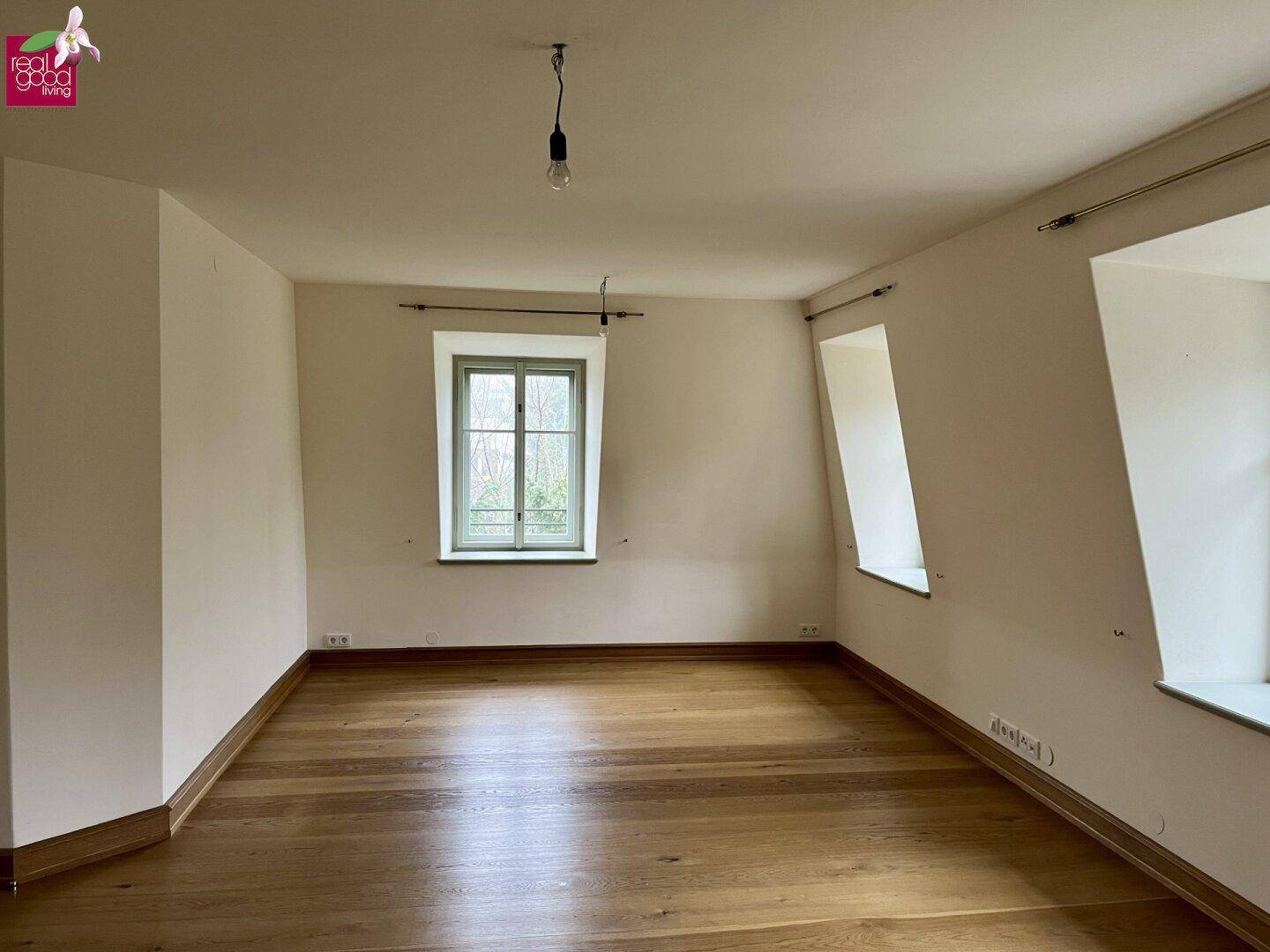 Helles Schlafzimmer mit Holzboden, Dachschrägen und großen Fenstern.