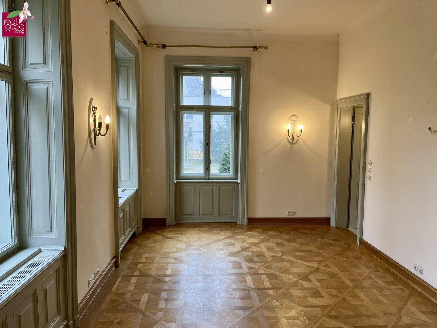 Geräumiger Raum mit Parkettboden, hohen Decken und großen Fenstern.