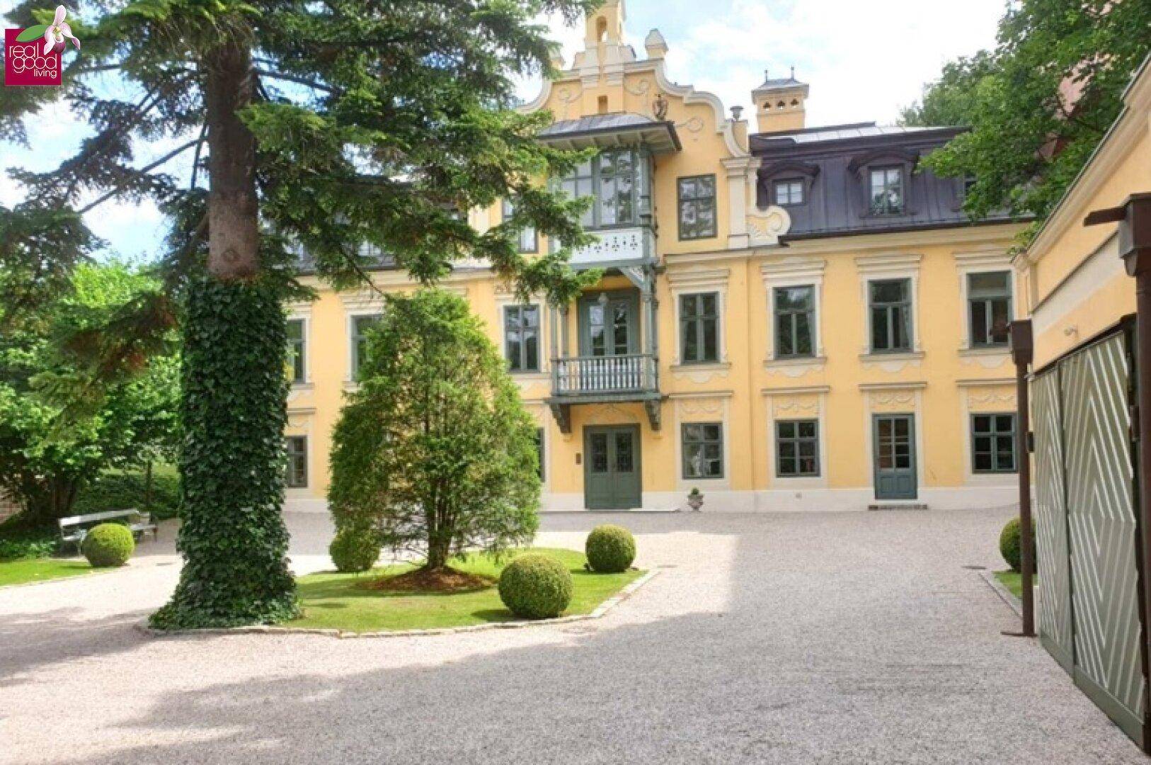 Großzügige Auffahrt zu einer eleganten Villa mit gepflegtem Vorgarten und altem Baumbestand.