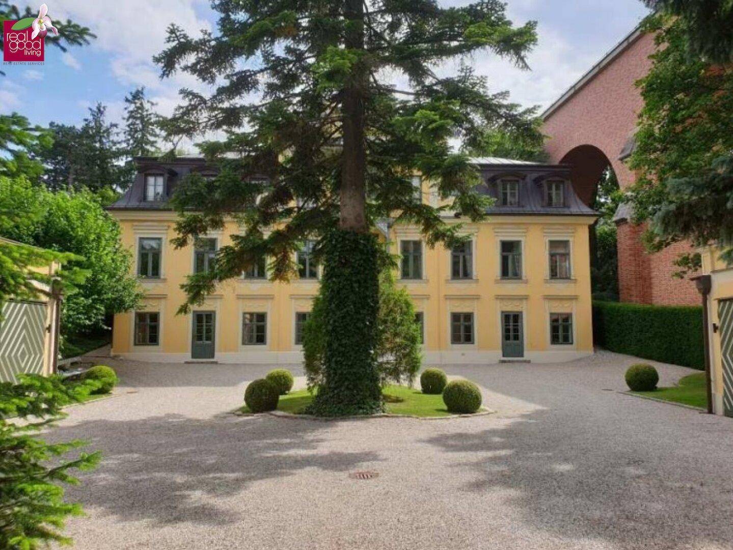 Repräsentative Vorderansicht der Villa mit breiter Kiesauffahrt und altem Baumbestand.