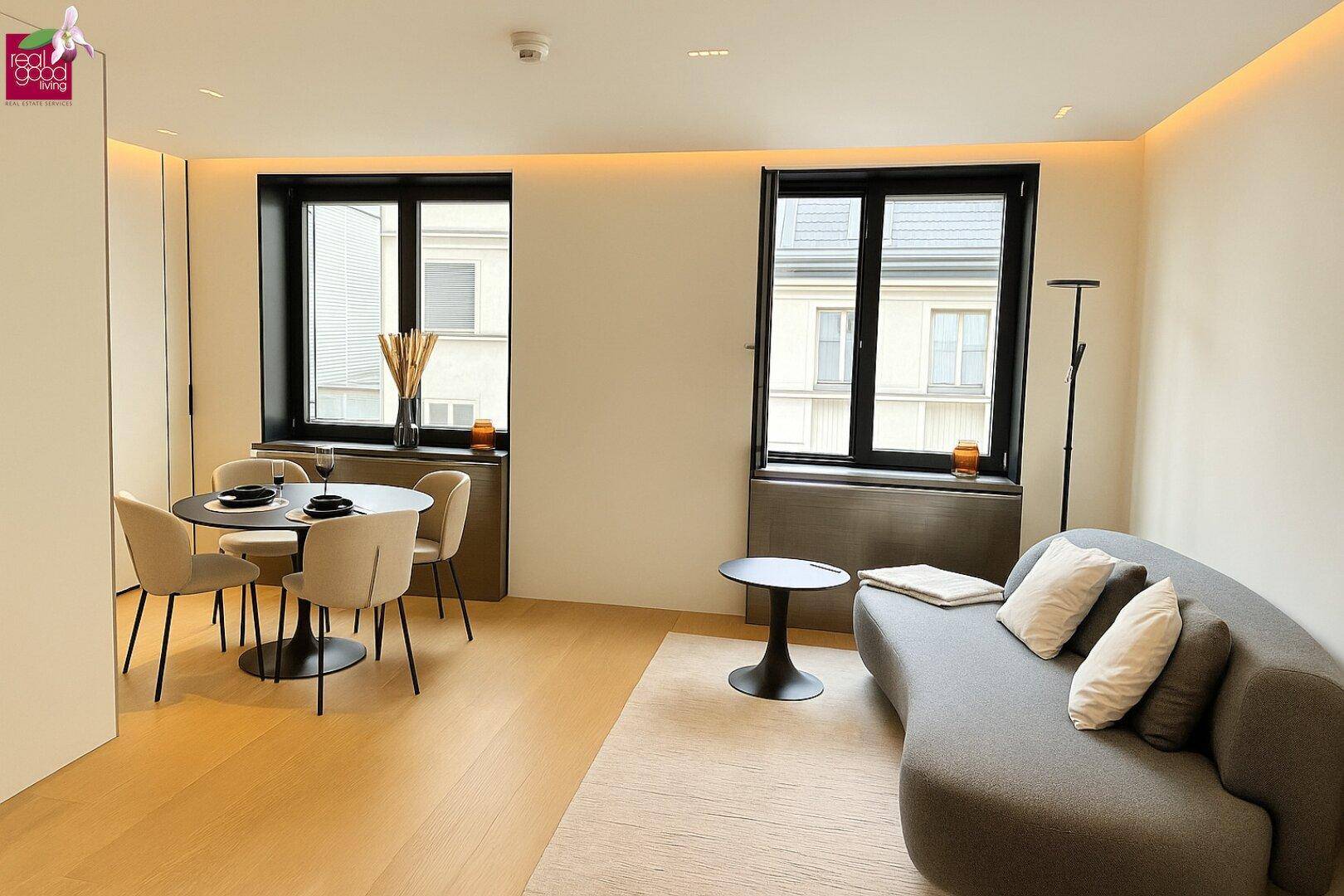 Gemütlicher Wohnbereich mit geschwungenem Sofa und großen Fenstern.