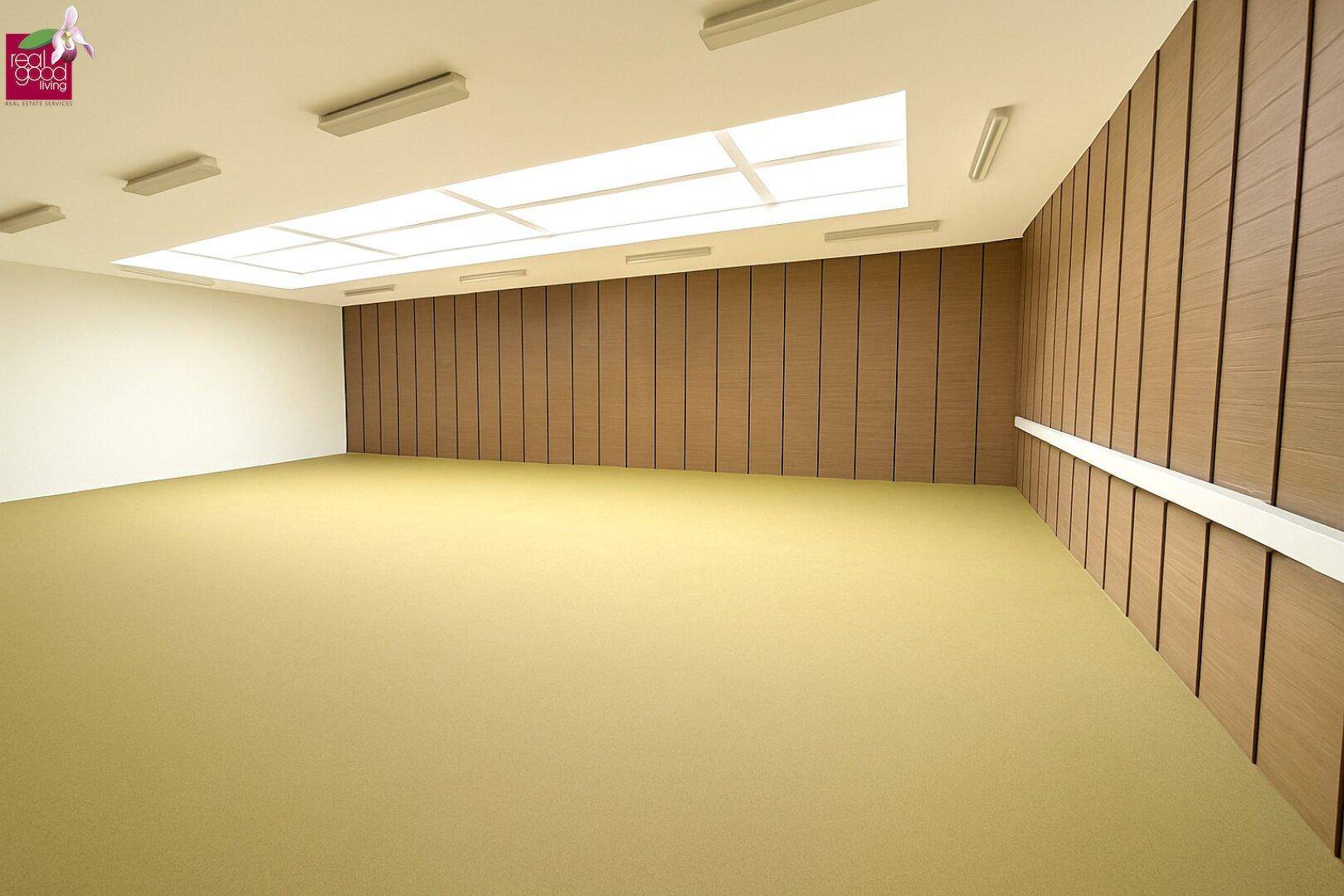 Großer, leerer Raum mit Holzvertäfelung und Deckenbeleuchtung, ideal für Konferenzen oder Veranstaltungen.