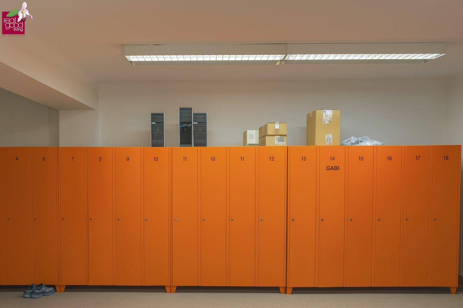 Umkleideraum mit einer langen Reihe orangefarbener Spinde und Lagerboxen auf den Schränken.