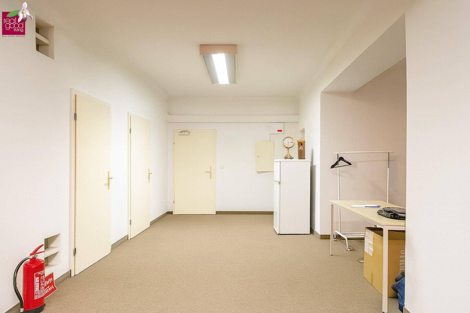 Langer Flur oder Lagerraum mit mehreren Türen, Teppichboden und einem Feuerlöscher.