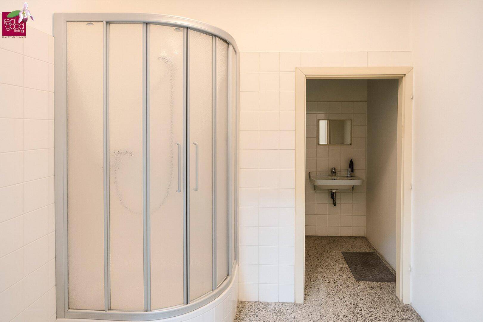 Badezimmer mit einer runden Duschkabine und einem separaten Bereich mit Waschbecken und Spiegel.