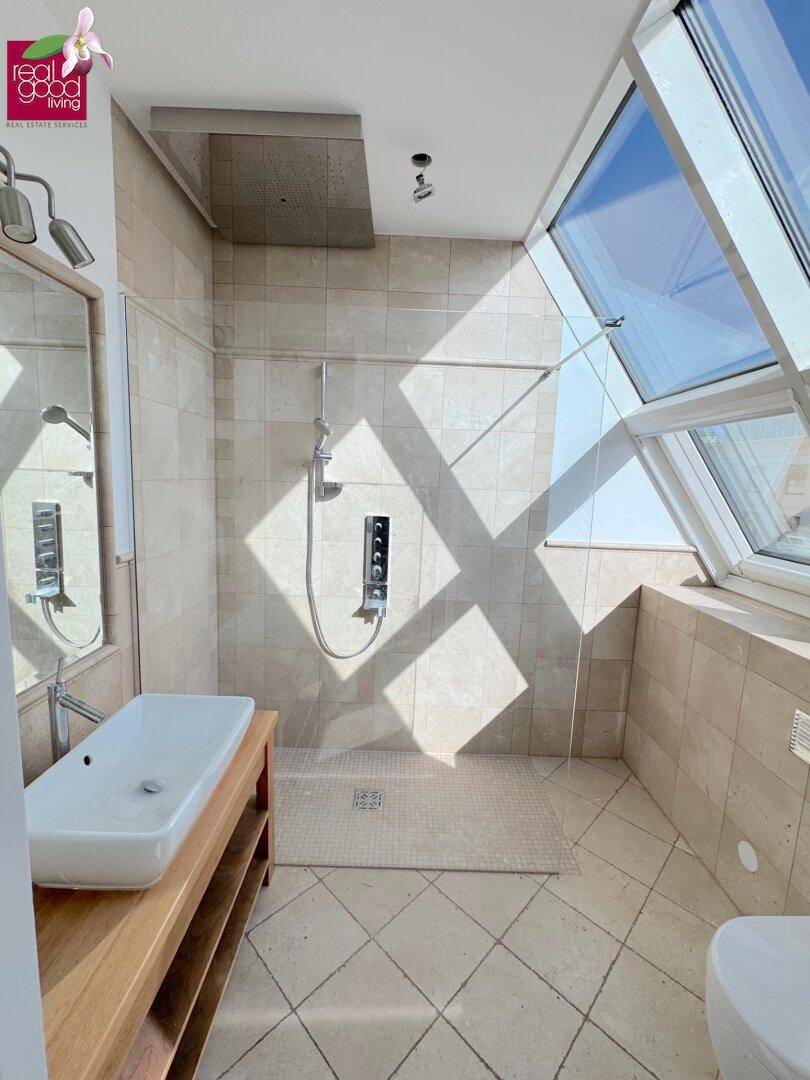 Modernes Badezimmer mit ebenerdiger Dusche, Holzwaschtisch und großen Dachfenstern für viel Licht.