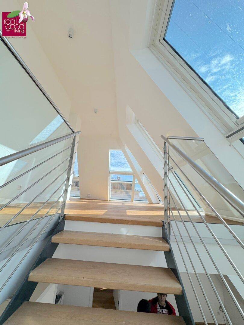 Moderne Treppe mit Glasgeländer und Holzstufen, umgeben von großen Dachfenstern für viel Tageslicht.