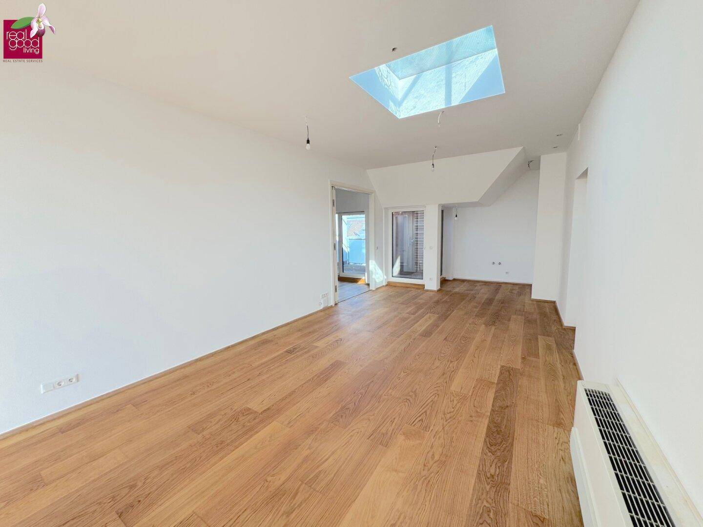 Geräumiger, heller Raum mit Holzboden, weißen Wänden und einem großen Oberlicht für viel Tageslicht.