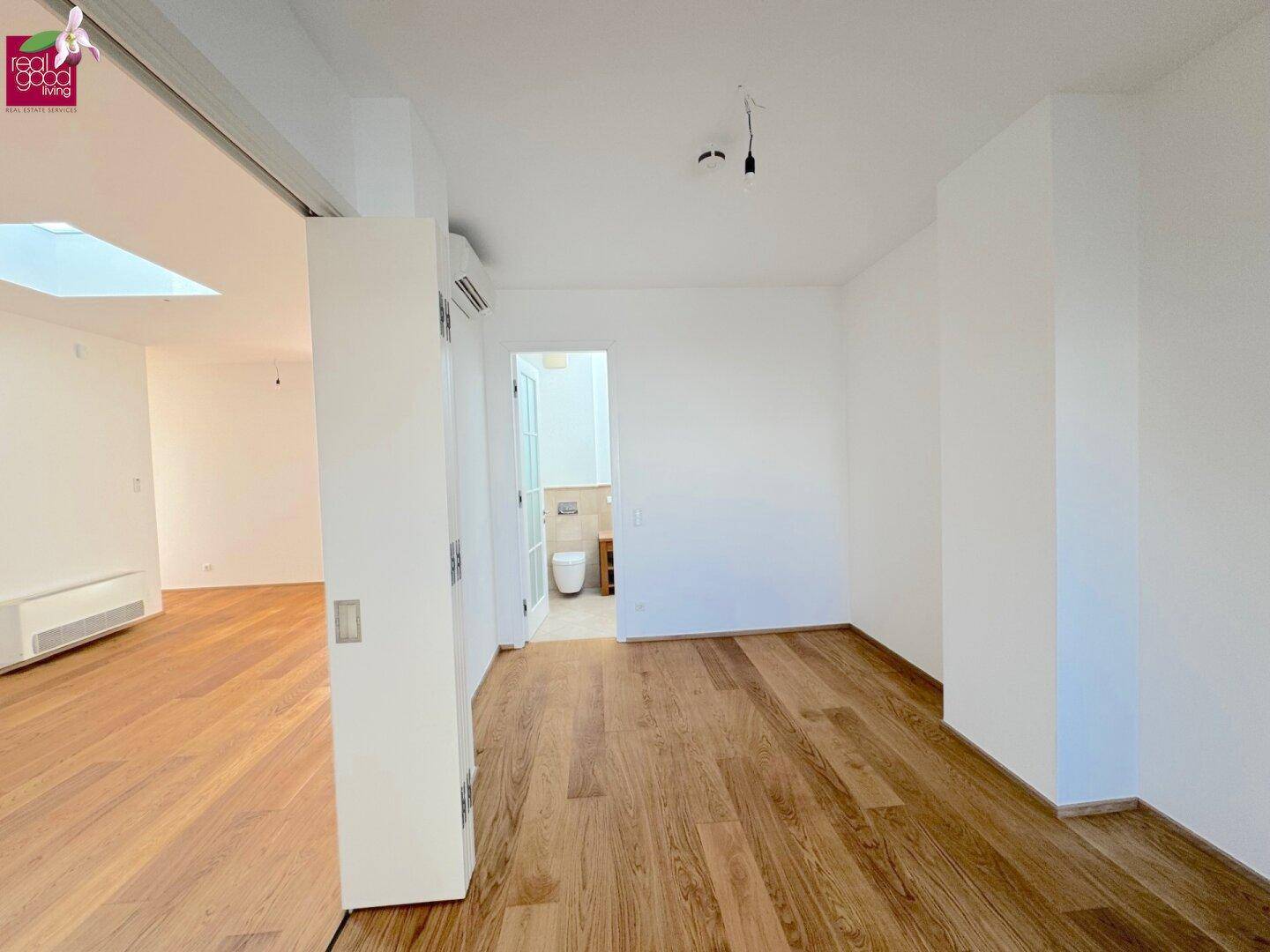 Heller Raum mit Holzboden und Zugang zu einem Badezimmer oder Gäste-WC, ideal als Schlafzimmer.