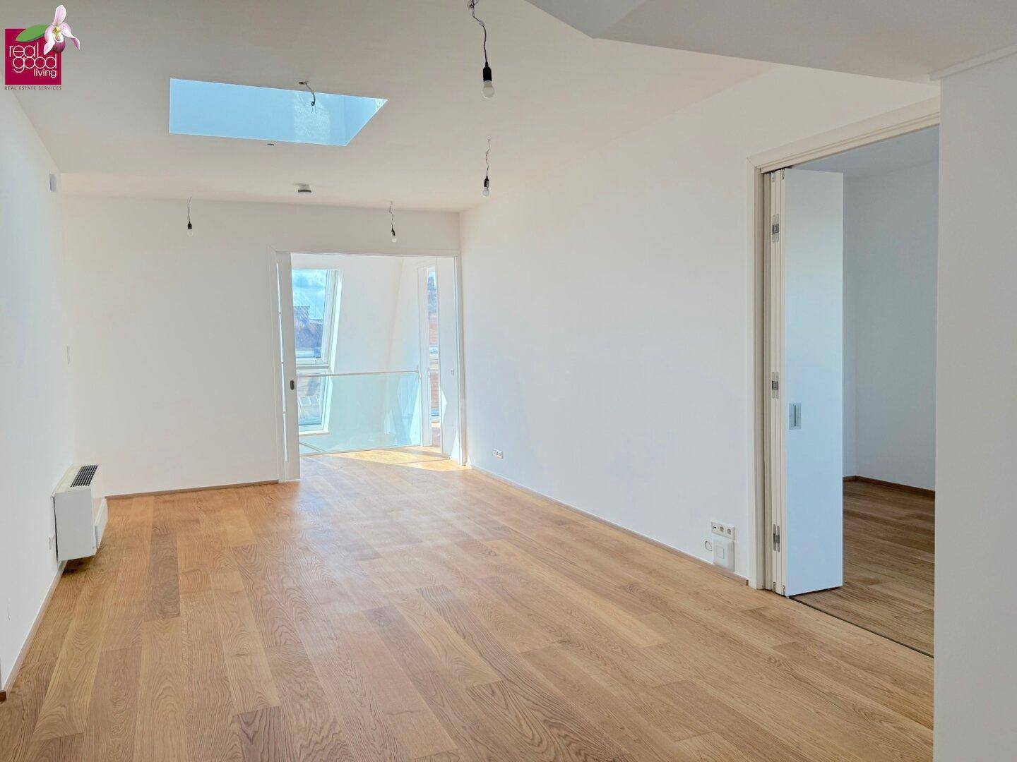 Offener Wohnbereich mit Holzboden, Oberlicht und Blick in einen angrenzenden Raum mit Dachfenstern.