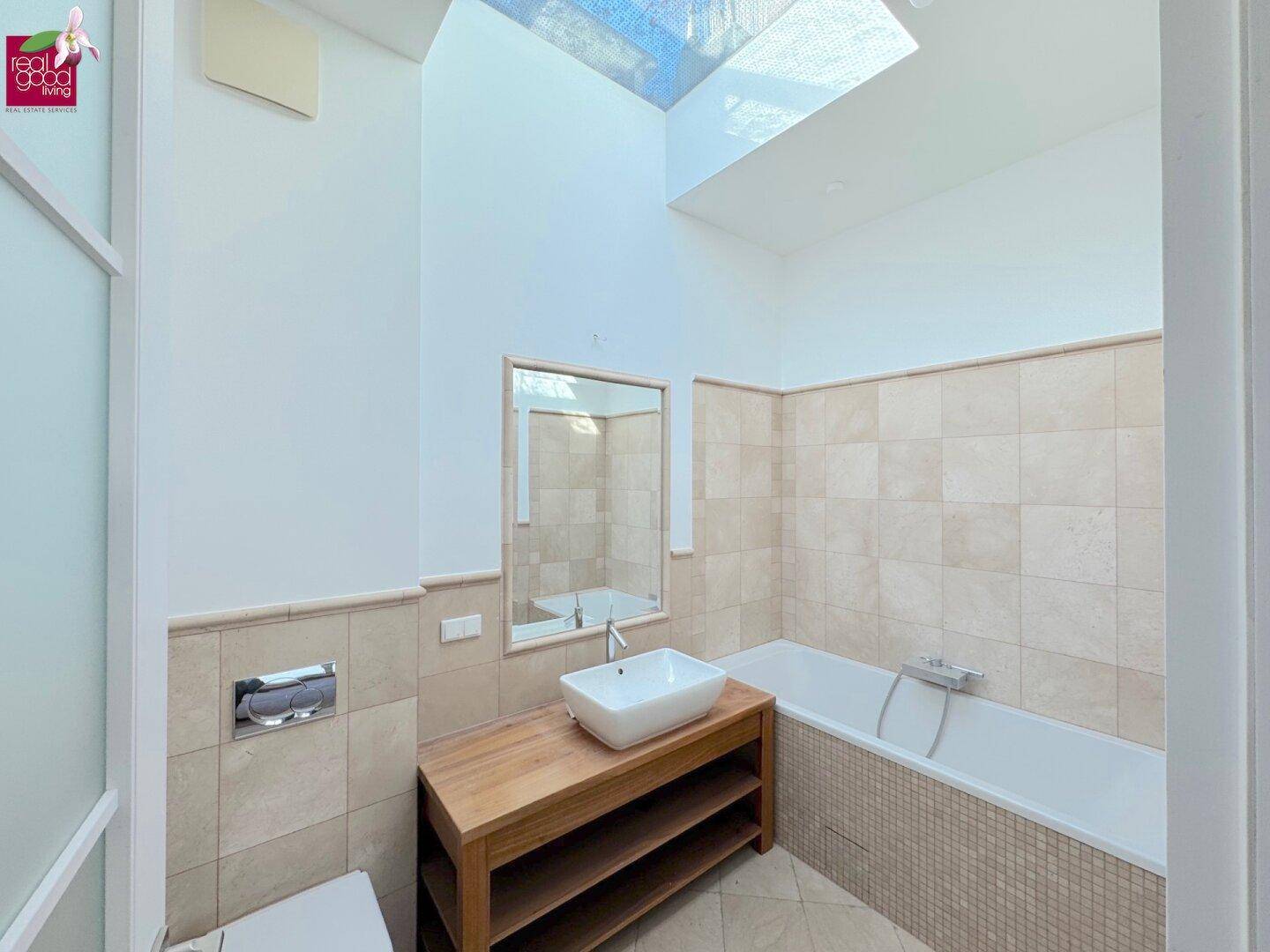 Helles Badezimmer mit Badewanne, modernem Waschbecken auf Holzunterschrank und Oberlicht.