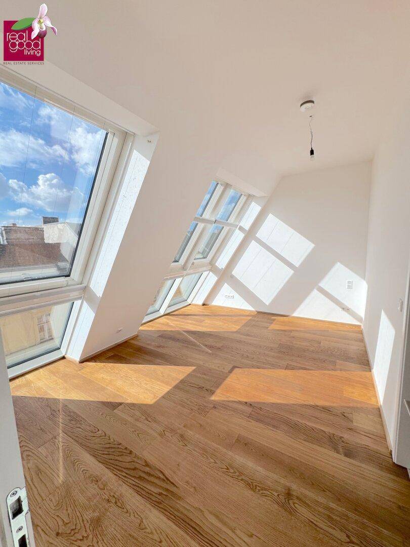 Lichtdurchflutetes Schlafzimmer mit Holzboden, großen Dachfenstern und schrägen Wänden.