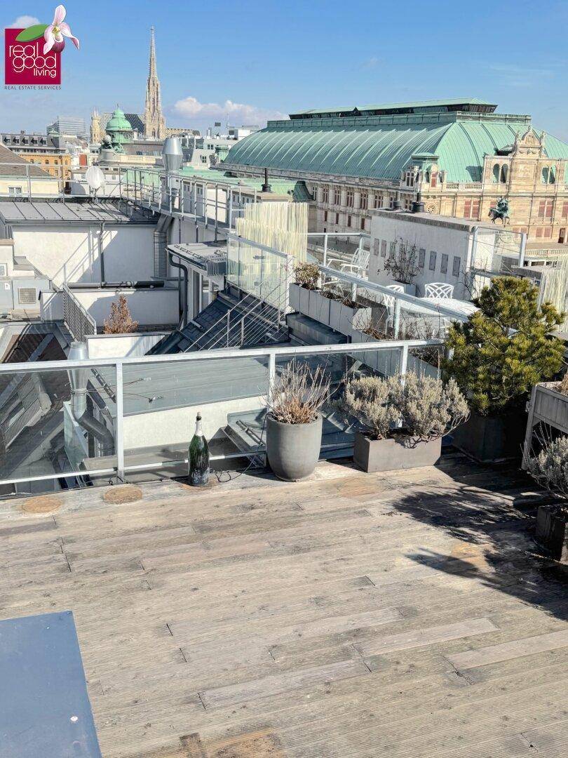 Sonnige Dachterrasse mit Holzbelag, Glasbrüstung und weitem Blick über die Dächer der Stadt.