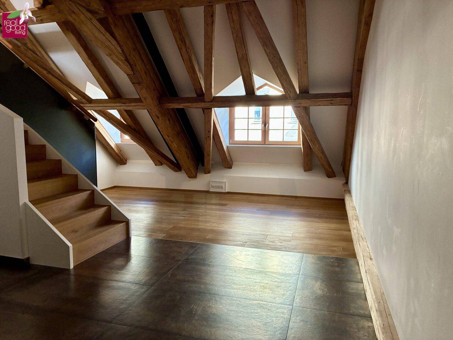 Heller Dachbodenraum mit sichtbaren Holzbalken, Holzfußboden und einer Treppe.