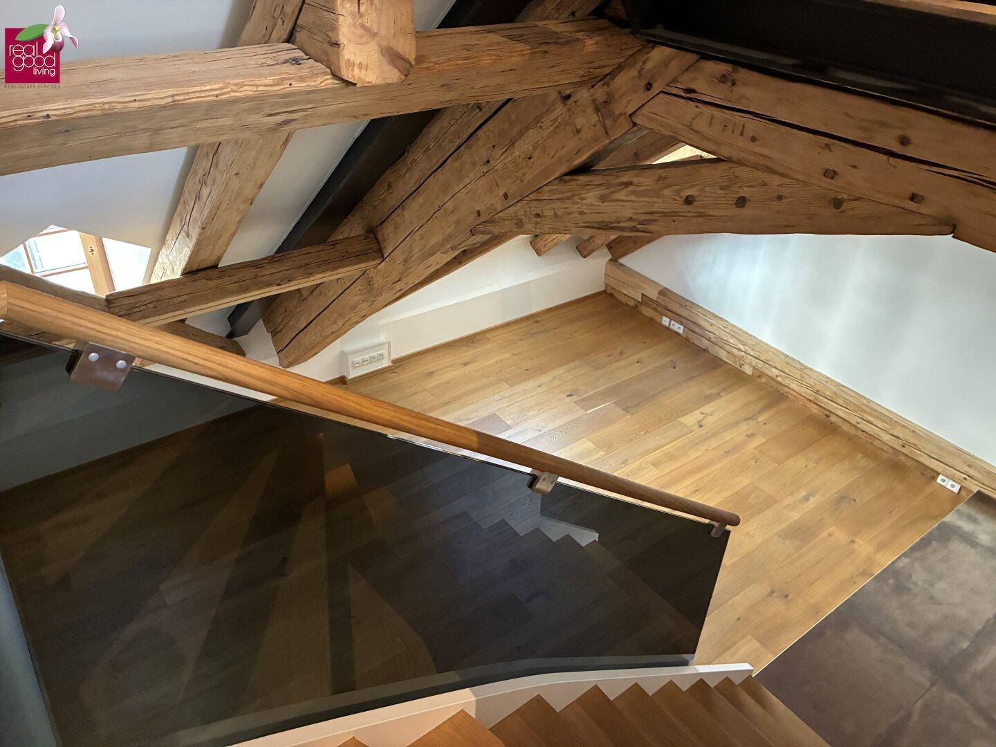 Holztreppe mit Glasgeländer und Blick auf den offenen Dachbodenbereich.
