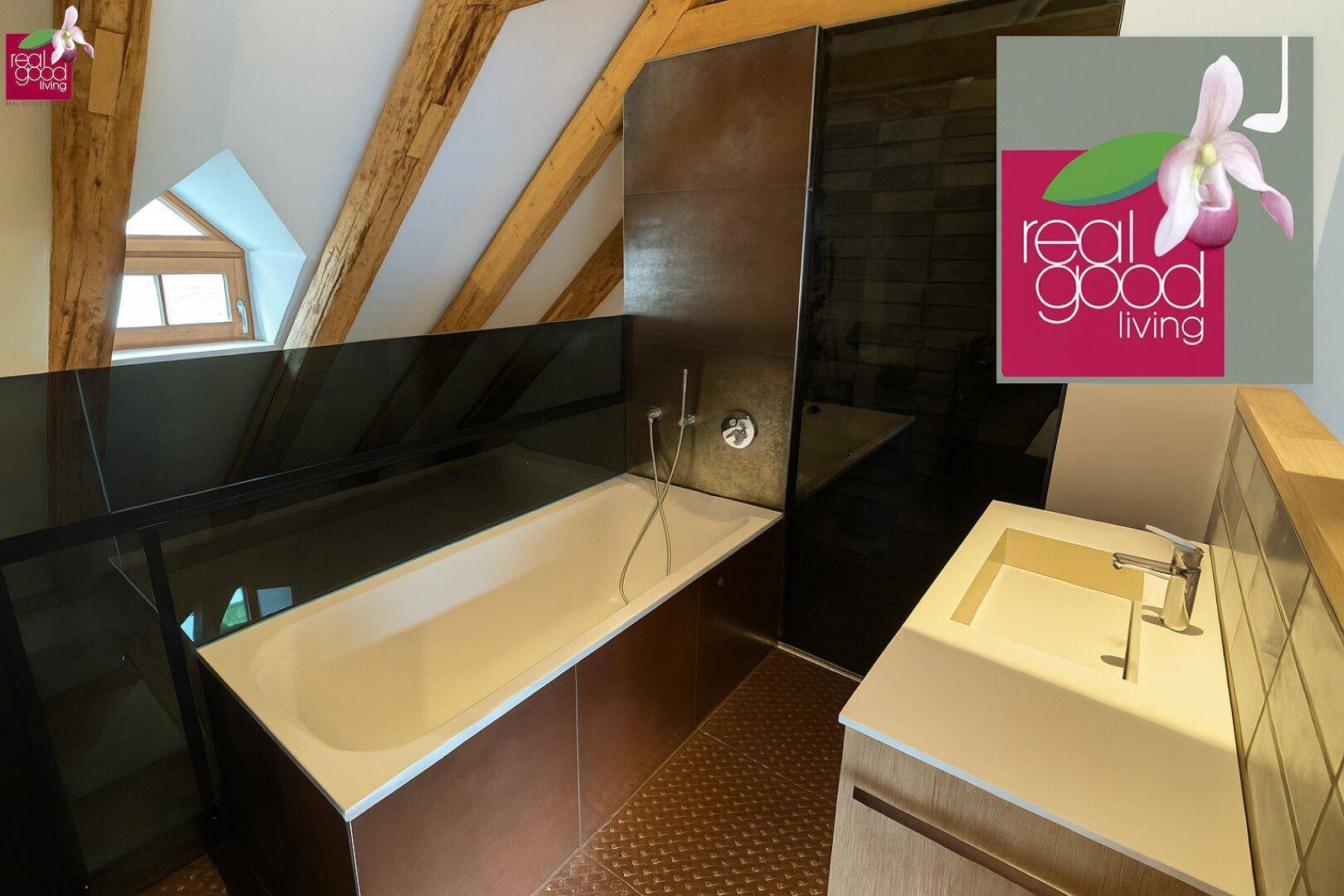 Modernes Badezimmer mit Badewanne, Waschbecken und dunklen Fliesen im Dachgeschoss.