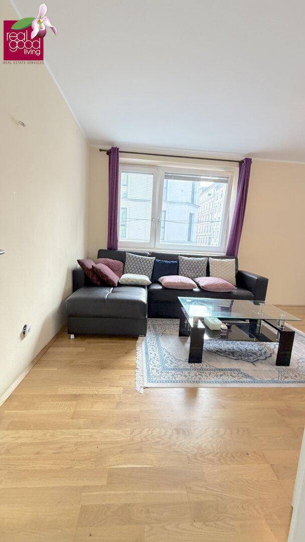 Gemütliches Wohnzimmer mit Ecksofa, Glas-Couchtisch und großen Fenstern mit Blick auf die Stadt.