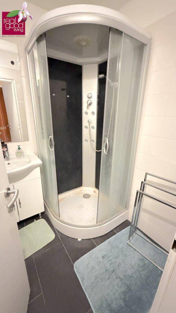 Badezimmer mit moderner Duschkabine, Waschbecken und dunklen Bodenfliesen in einem funktionalen Design.