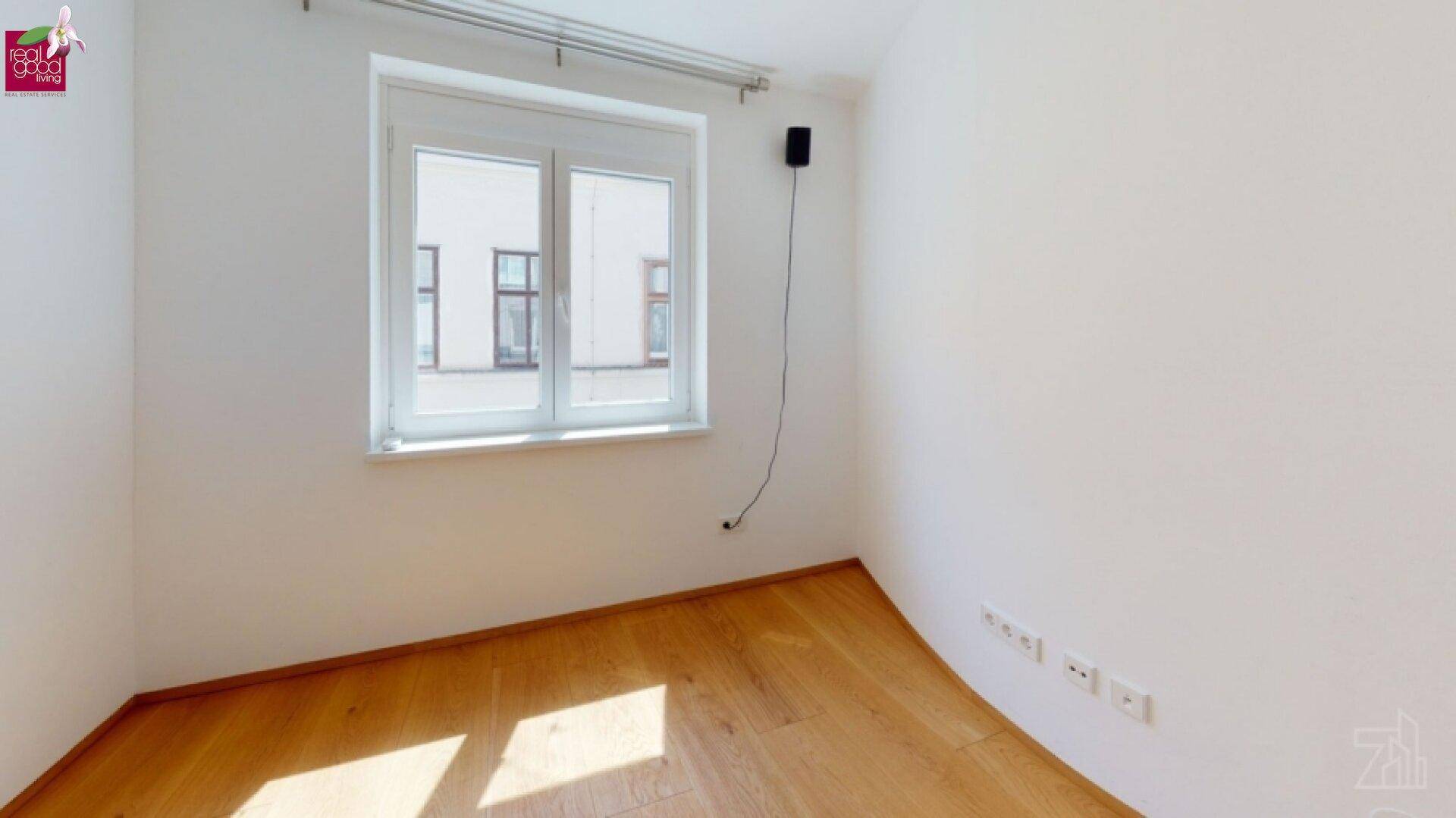 Heller Raum mit Parkettboden und großem Fenster, ideal für verschiedene Nutzungen.