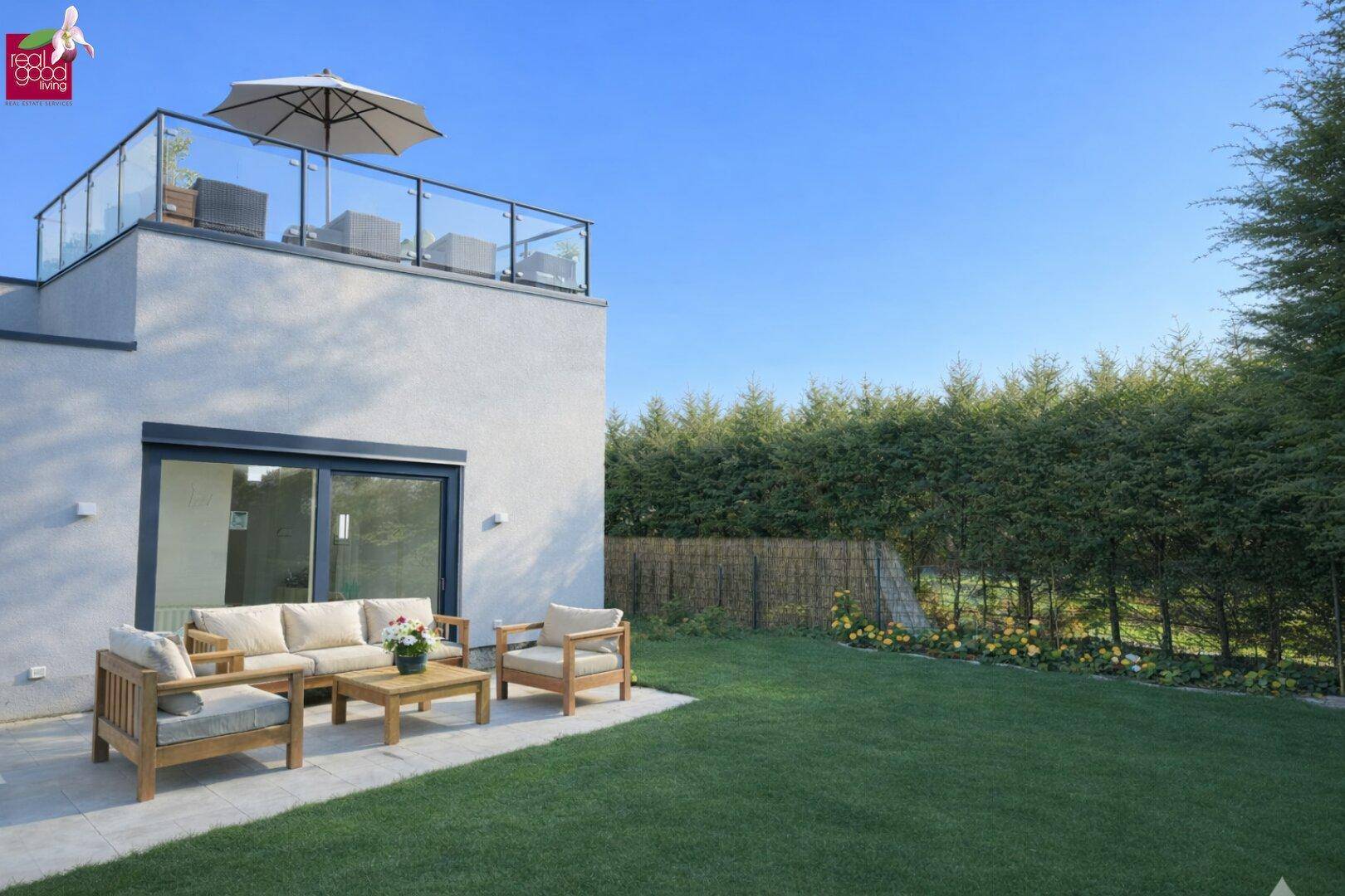 Moderne Hausfassade mit möblierter Terrasse, Rasenfläche und einer Dachterrasse mit Sitzgelegenheiten.