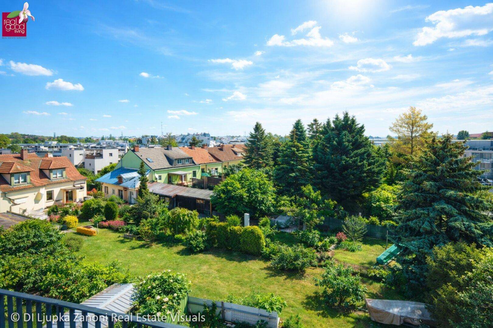 Weitläufiger Blick über eine grüne Wohngegend mit vielen Bäumen und Häusern unter blauem Himmel.
