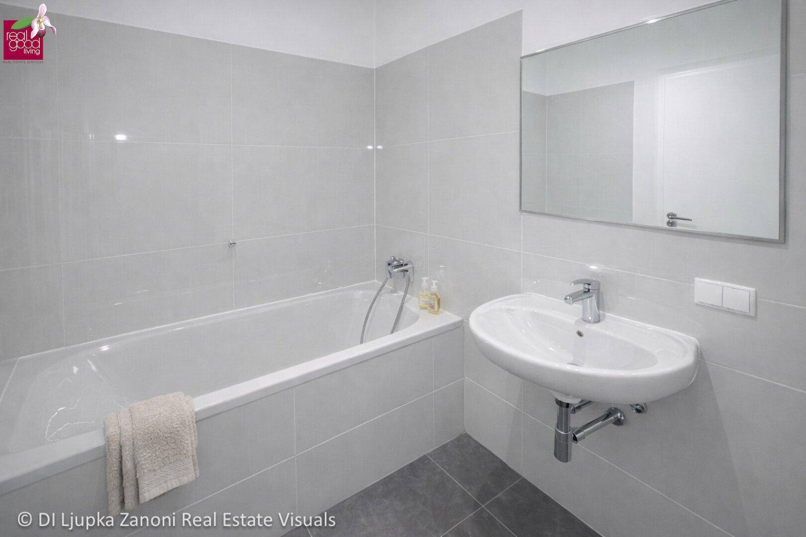 Modernes Badezimmer mit hellgrauen Fliesen, Badewanne und Wandwaschbecken.