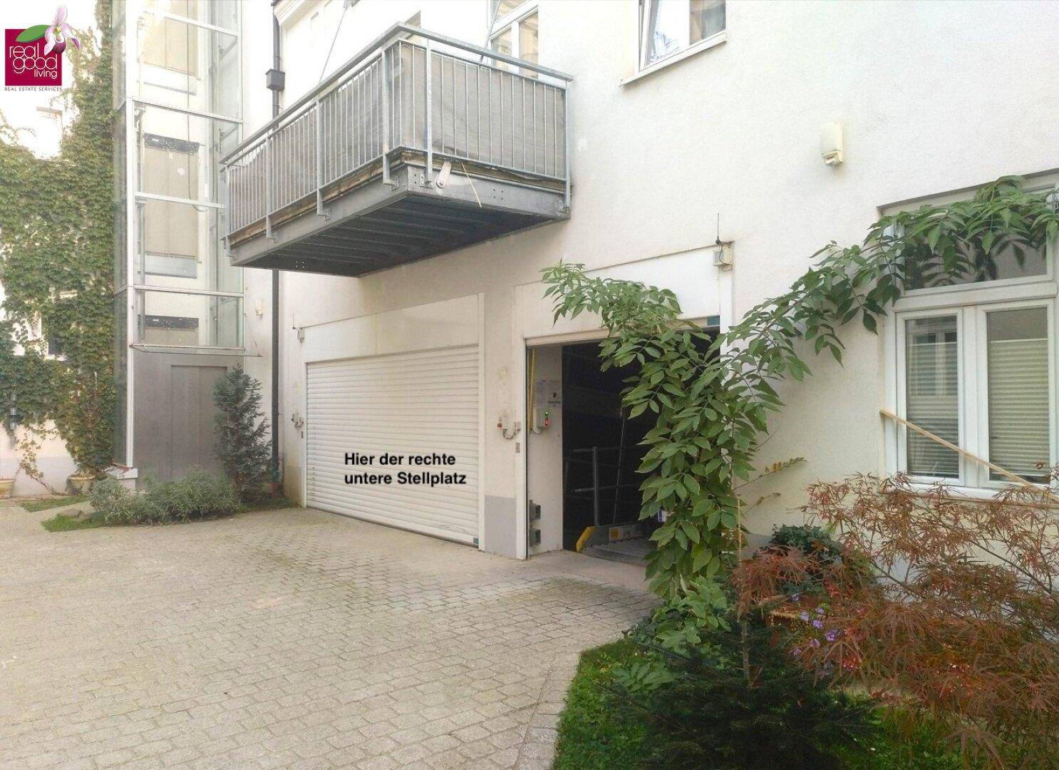 Außenansicht des Gebäudes mit Balkon, Außenaufzug, Garagentor und gepflastertem Stellplatz.