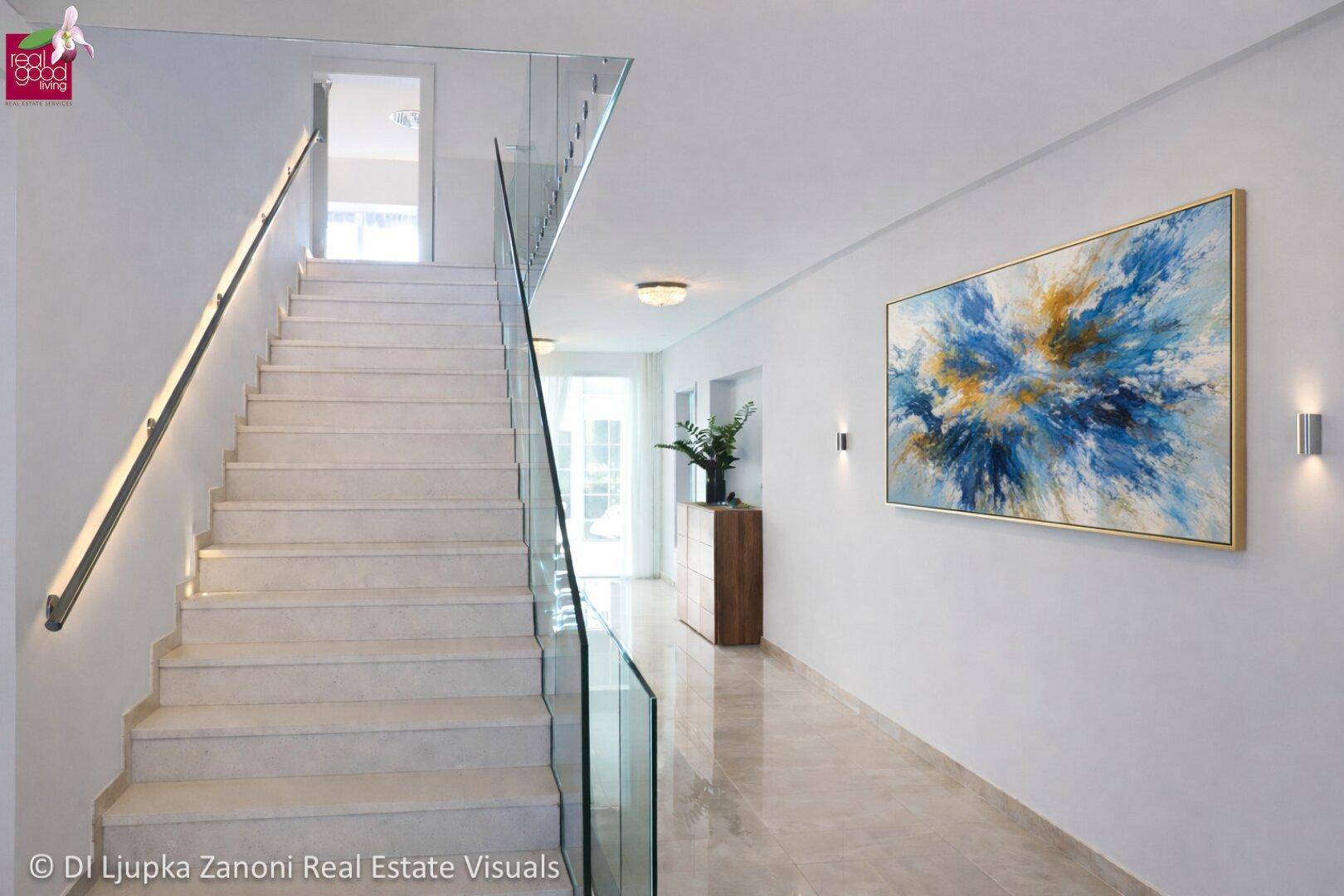 Elegantes Treppenhaus mit Glasgeländer, moderner Beleuchtung und einem farbenfrohen Kunstwerk.