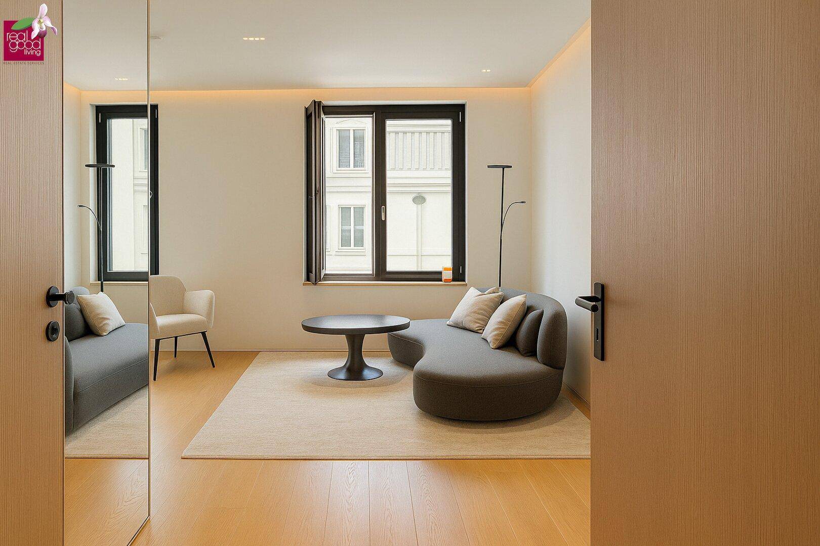 Helles Wohnzimmer mit modernem Sofa, Holzboden und großen Fenstern, die viel Tageslicht hereinlassen.