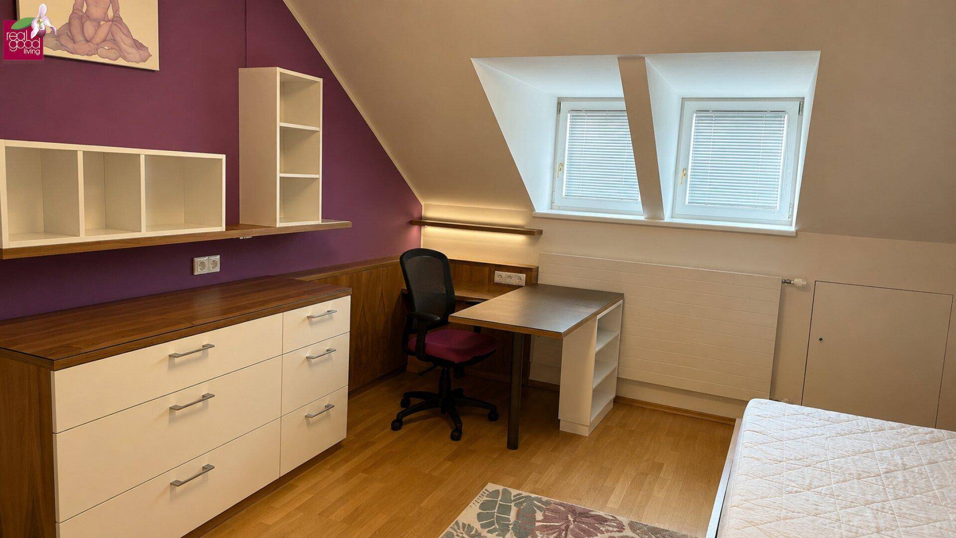 Arbeitsbereich im Dachgeschoss mit Schreibtisch, Regalen und Dachschrägenfenstern.
