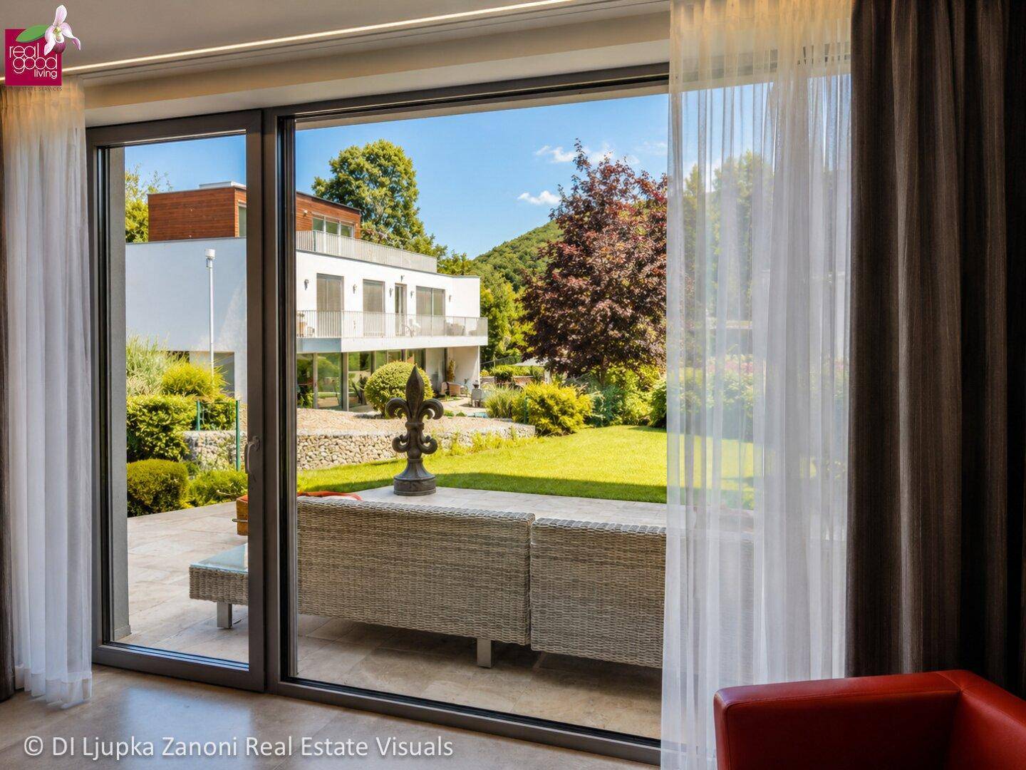 Weitläufiger Blick aus dem Wohnzimmer auf den Garten und die moderne Architektur des Nachbargebäudes.